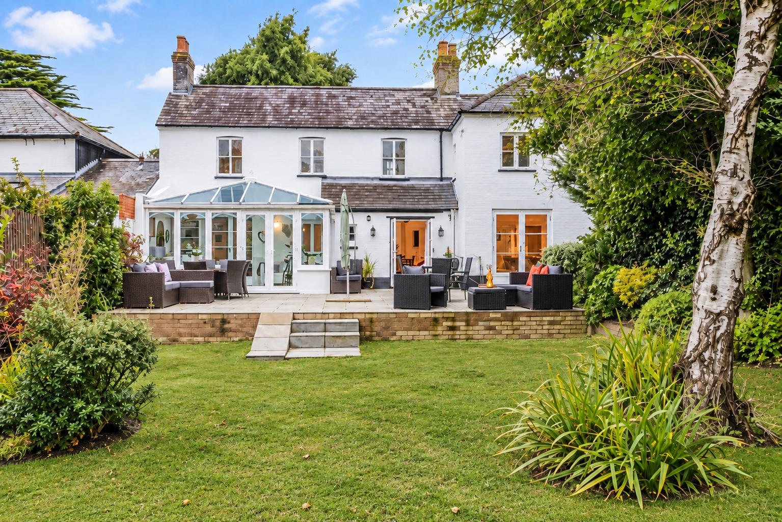 Victoria Cottage viewed from across the garden, showing the full white-painted exterior and conservatory