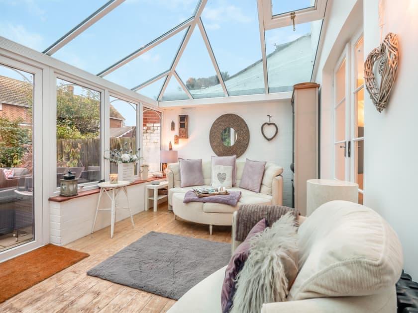 Glass-roofed conservatory with soft seating, opening onto the garden